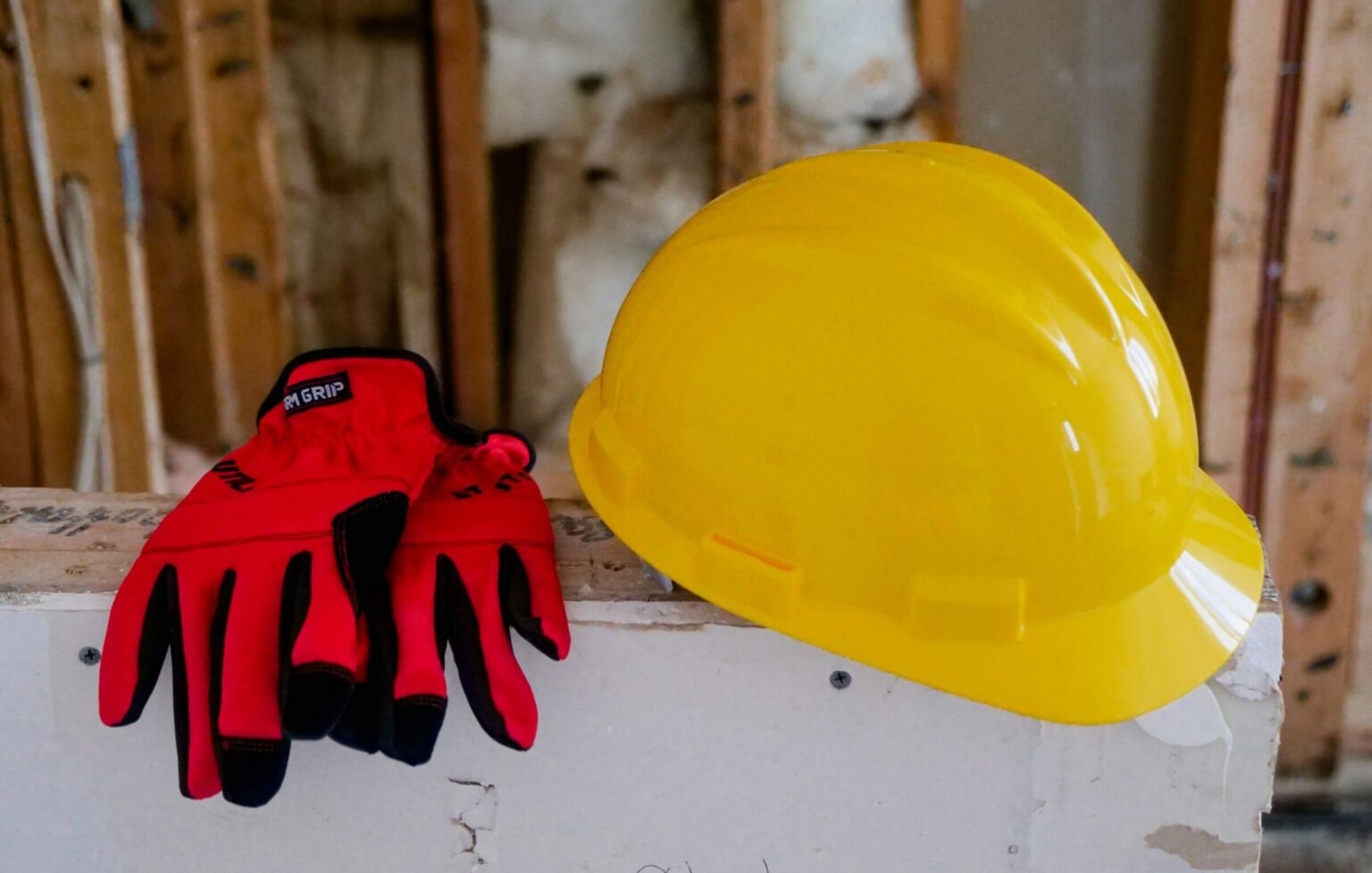 Close-up of a yellow hard hat and red gloves on a construction site, symbolizing safety and work.